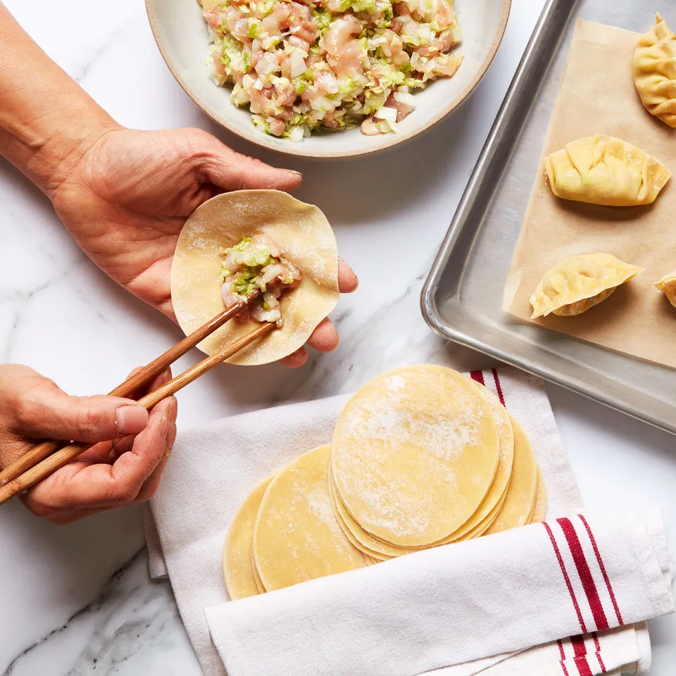 A person using a pair of chopsticks to place a small mound of savory filling onto a dumpling wrapper 