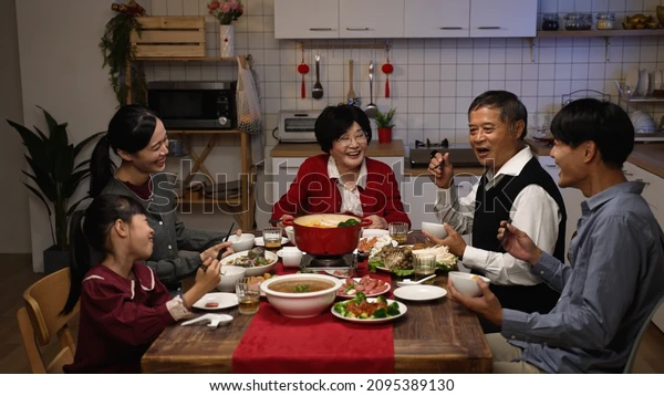 Happy family gathered around a dining table, sharing food and smiling together in a warm tradition of communal eating and togetherness.